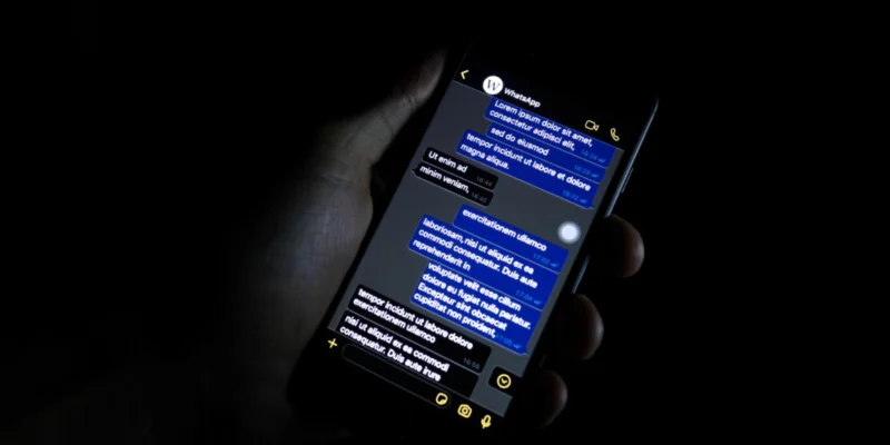 Hand holding a smartphone showing a messaging app conversation in a dark room