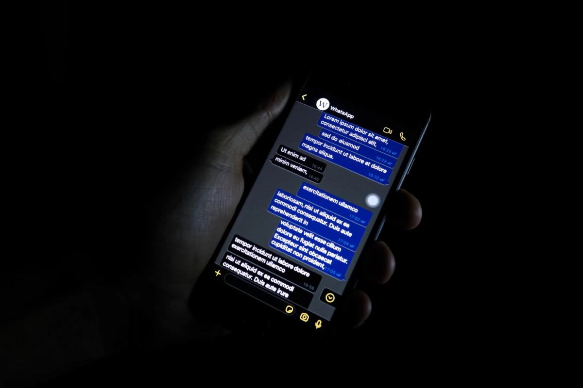 Hand holding a smartphone showing a messaging app conversation in a dark room